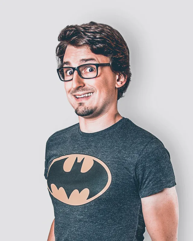 Andreas Zeitler mit Brille und Batman-T-Shirt vor hellgrauem Hintergrund